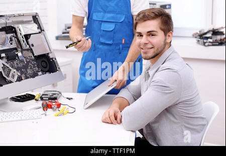 Master showing the repair process to young man in service center Stock Photo