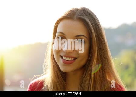 Close-up portrait of beautiful young adult woman in the sunlight at sunset. Pretty smiling girl. Beautiful woman is enjoying warm and sunlight.