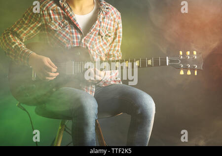 Young man playing electric guitar on lighted foggy background Stock Photo