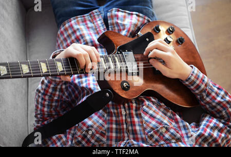 Young man playing electric guitar on grey sofa at home Stock Photo