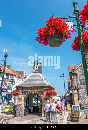 People walking in Sheringham town centre on a hot summer day, with the historic clock building from 1862 providing shade. North Norfolk, England, UK. Stock Photo