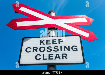 A level crossing (where a road crosses a railway line) signpost, with the notice – Keep crossing clear, against a blue sky. Norfolk, England, UK. Stock Photo