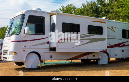 Side view of white Damon Daybreak motorhome / RV, parked up on a UK campsite, with slide out room in use, and the front wheels raised off the ground. Stock Photo