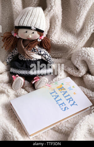 Rag doll with fairy tales book on  bedspread. Childhood concept Stock Photo