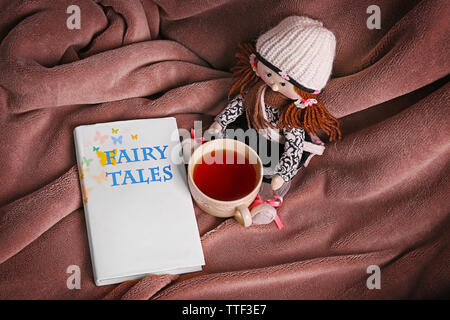 Rag doll with fairy tales book  and cup of tea on bedspread. Childhood concept Stock Photo
