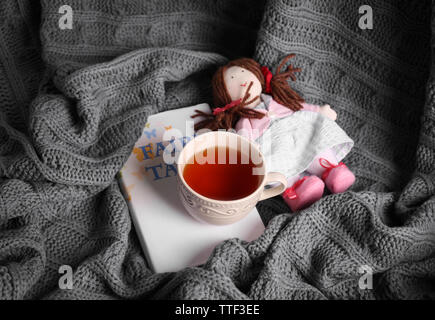 Rag doll with fairy tales book and cup of tea on bedspread. Childhood concept Stock Photo
