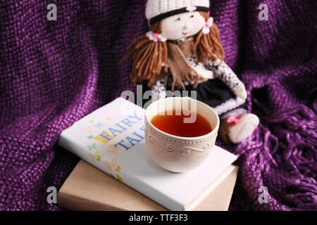 Rag doll with fairy tales books and cup of tea on bedspread. Childhood concept Stock Photo