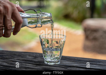 A waiter in a restaurant pours fresh water from a bottle into a glass, close up, outdoors Stock Photo