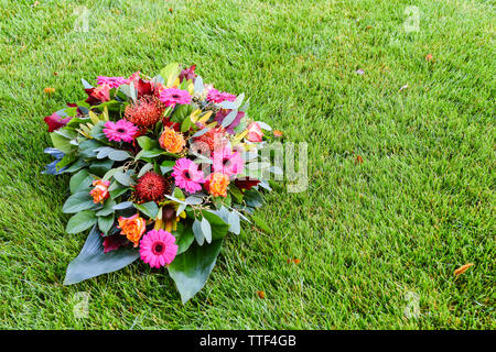 Pink and orange colored flower arrangement on lawn. All Saints day flower arrangements, flowers for grave and funeral. Floral backgrounds for mourning Stock Photo
