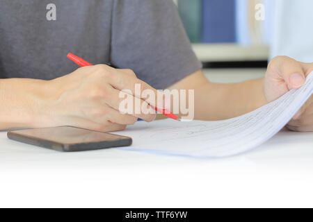 Closeup human hand checking work on a paper. freelance man writing with red pen on paper work. man in office  drawing on notepad with smartphone Stock Photo