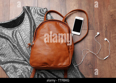 Brown leather backpack with female items on wooden surface, top view Stock Photo