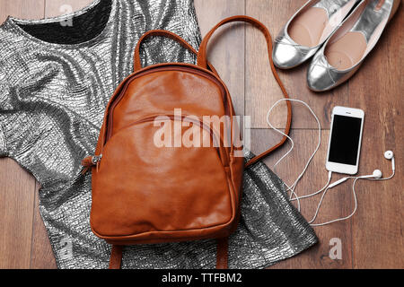 Brown leather backpack with female items on wooden surface, top view Stock Photo