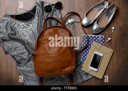 Brown leather backpack with female items on wooden surface, top view Stock Photo