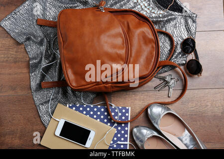 Brown leather backpack with female items on wooden surface, top view Stock Photo