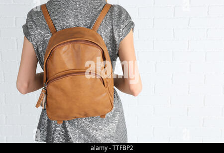 Back of woman with brown leather backpack against white brick wall background Stock Photo