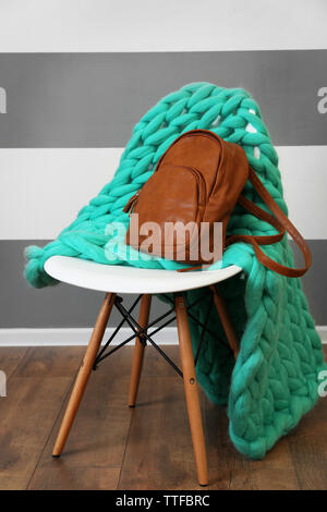 Brown leather backpack with knitted plaid on chair indoors Stock Photo