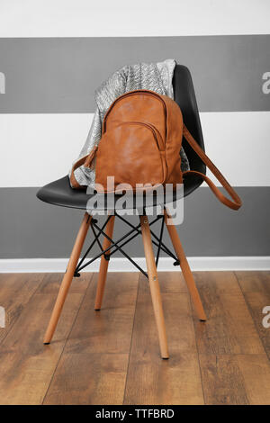 Brown leather backpack and shirts on chair indoors Stock Photo