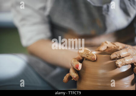Midsection of woman shaping clay on spinning wheel at workshop Stock Photo