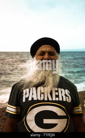 An old man with a long gray beard is standing by the sea. Stock Photo