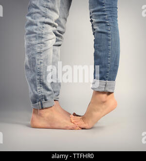 Young woman standing on the boyfriend's feet over grey background Stock Photo