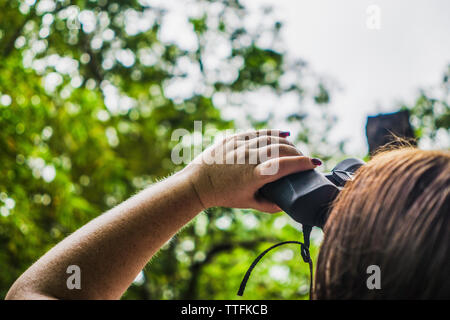 Cropped image of woman looking at trees through binoculars Stock Photo