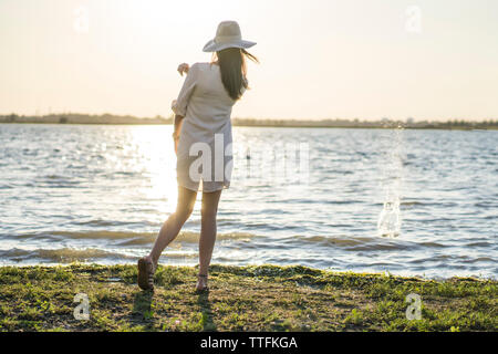 Beautiful young woman in dress along water with sunset behind Stock Photo