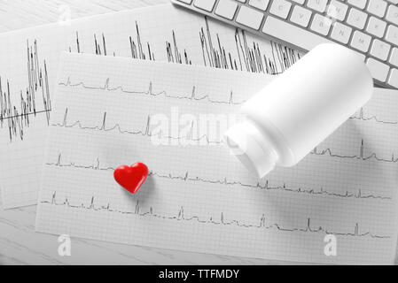 Cardiogram chart with small red heart and plastic bottle of medicines on table closeup Stock Photo