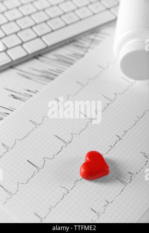 Cardiogram chart with small red heart and plastic bottle of medicines on table closeup Stock Photo