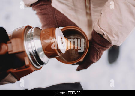 cropped hand of woman pouring coffee for wife in cup at park during winter Stock Photo