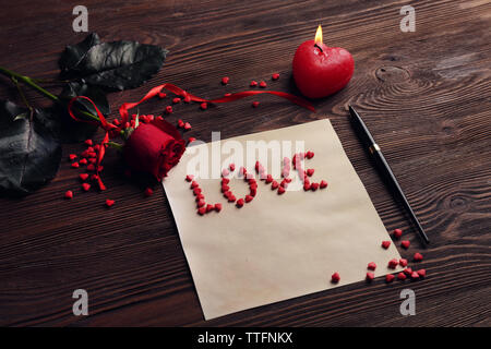 Gift card for Valentine's Day with love word, red rose, pen and candle on wooden background Stock Photo