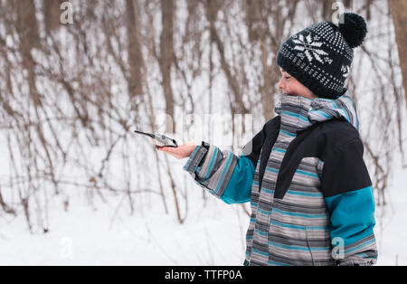 Boy happily feeding bird from his hand in wooded area on a winter day. Stock Photo