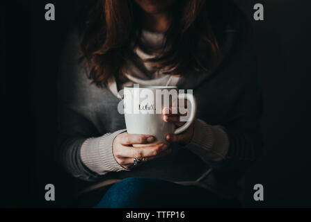 Woman holding a mug with the word relax on it in a darkened room. Stock Photo