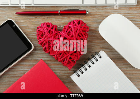 Computer peripherals with red wicker heart, notebooks and mobile phone on wooden table Stock Photo
