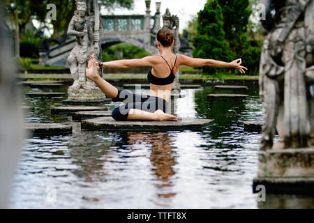 Full length of woman practicing yoga on platform amidst pond at park Stock Photo