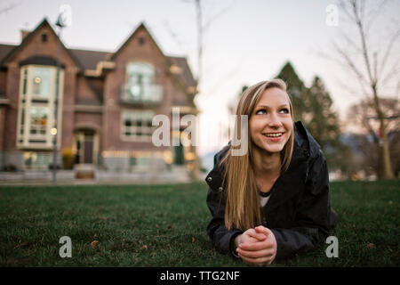 Smiling teenage girl looking up while relaxing on grassy field at yard during sunset Stock Photo