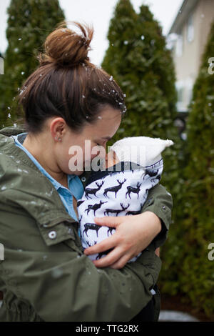 Mother rubbing noses with baby boy while carrying him at yard Stock Photo