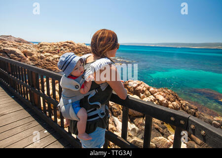 Mother carrying son in carriage while standing on pier against clear sky during sunny day Stock Photo