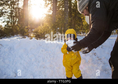 Father hands a snowball to his toddler son Stock Photo