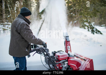 Side view of man using snow blower machine to clear driveway Stock Photo