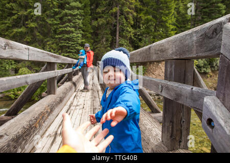 Toddler boy reaching for fathers hand, safely cross wooden bridge Stock Photo