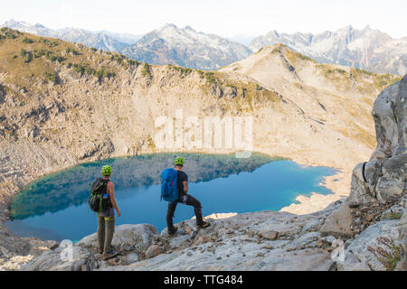 Mountaineers look down on alpine tarn and surrounding peaks. Stock Photo