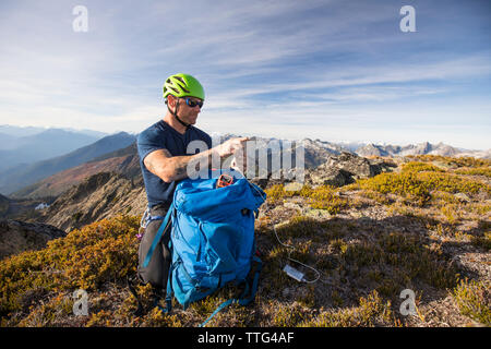 Climber charges his phone with battery pack on mountain summit. Stock Photo