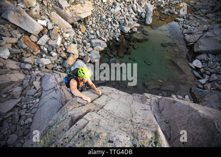 high angle of man bouldering above small alpine tarn. Stock Photo