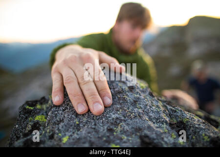 climbers hand grips a rock at the top of a bouldering route.