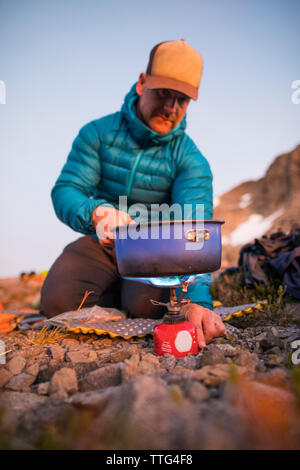 Mountaineer cooking a meal on an ultralight stove in the mountains. Stock Photo