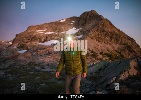 Mountaineer on the move, wearing headlamp at dusk in the mountains. Stock Photo
