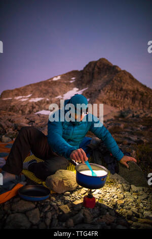 Backpacker cooking on camp stove and using headlamp at sunset Stock Photo
