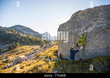 Climber bouldering on large rock with spotter below. Stock Photo