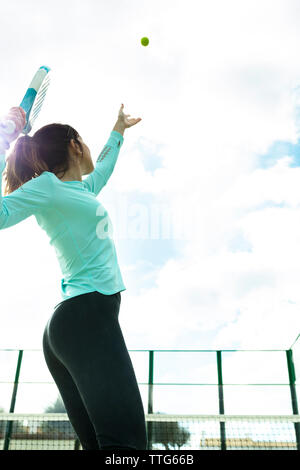 Low angle view of woman serving tennis ball against cloudy sky at court Stock Photo