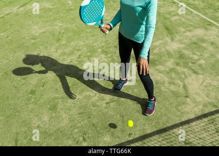 Low section of woman playing paddle tennis on court during sunny day Stock Photo
